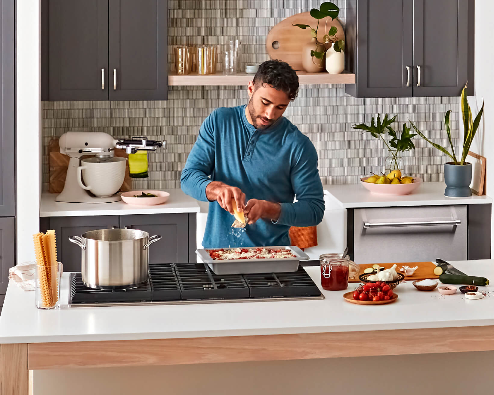 A person grating cheese over a lasagna over a KitchenAid® cooktop on an island.