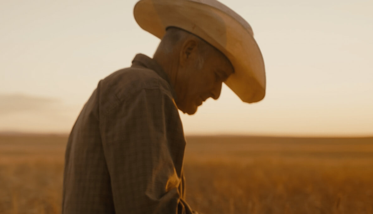 A man wearing a cowboy hat walking through a wheat field in Montana. 