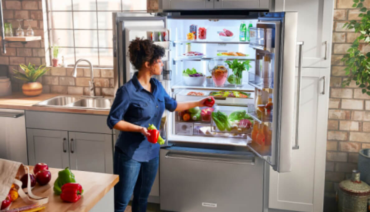 Woman loading vegetable into a french door refrigerator.