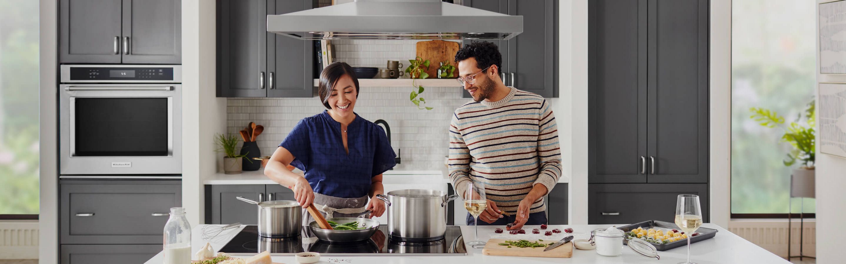 A woman and a man cooking on a KitchenAid® cooktop. 