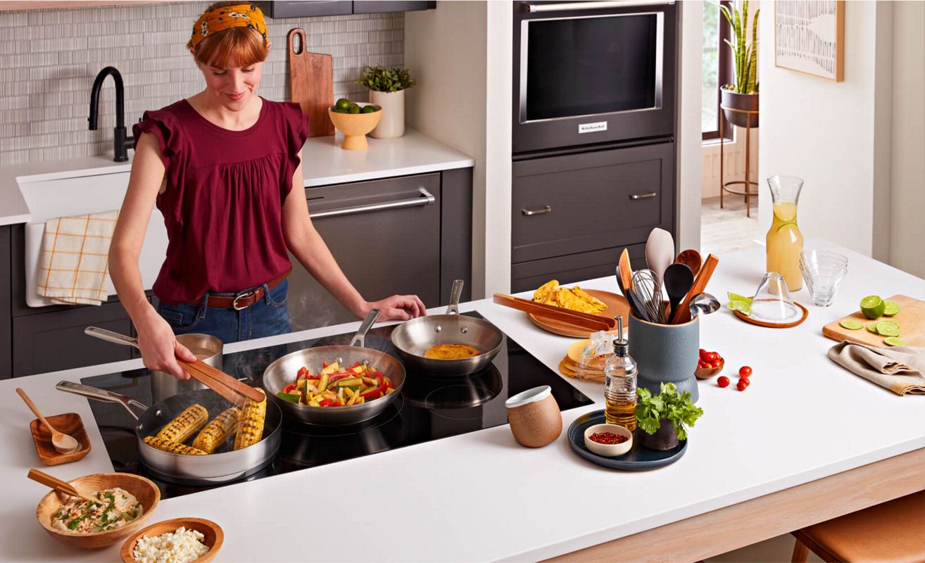 A person cooking with multiple pans on an induction cooktop.
