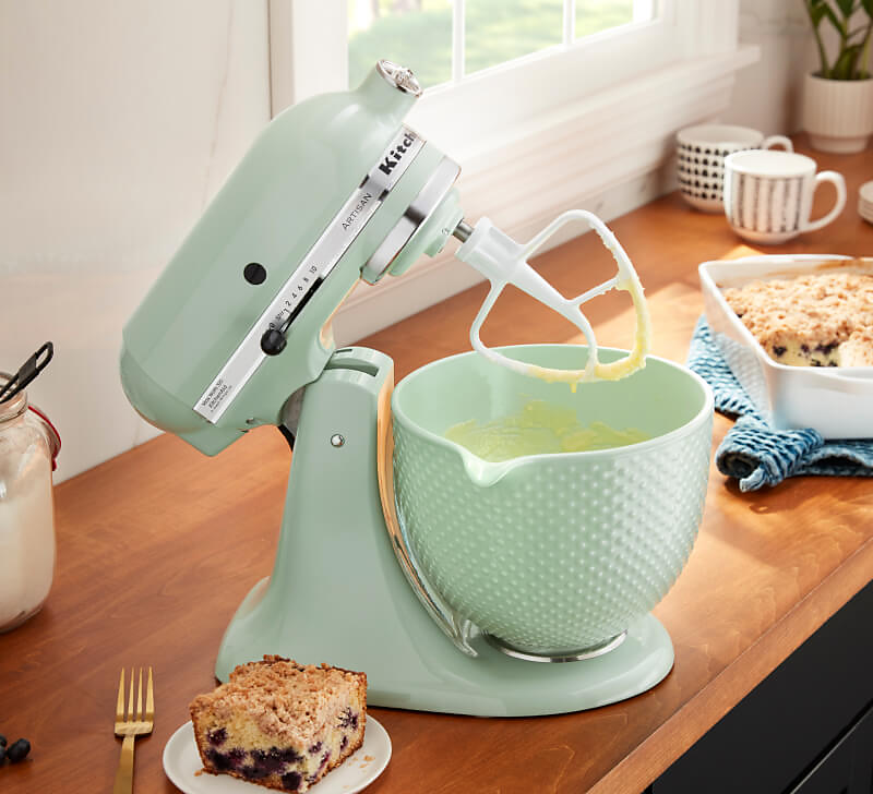 A Dew Drop stand mixer and bowl, with the head tilted mixing batter. 