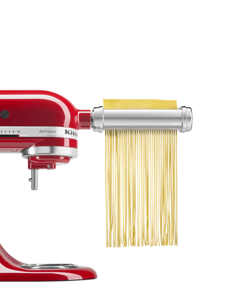 Red stand mixer with pasta and grain attachment cutting pasta sheets in linguine shape.