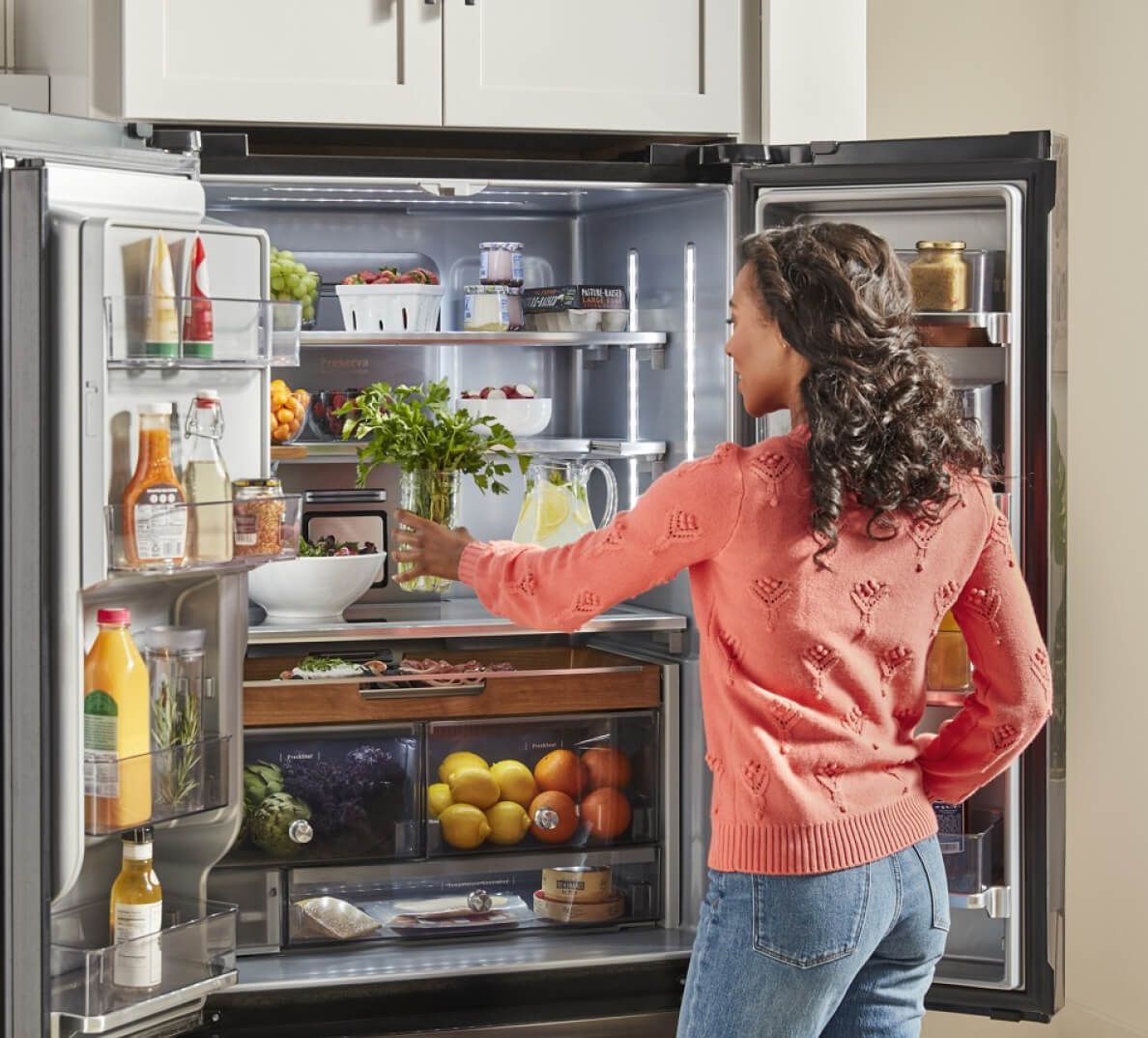 Woman reaching for produce in organized refrigerator.