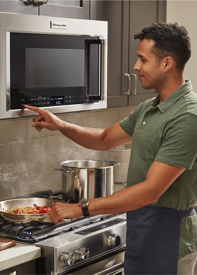 A man activating the ventilation system on his over-the-range microwave hood combination.