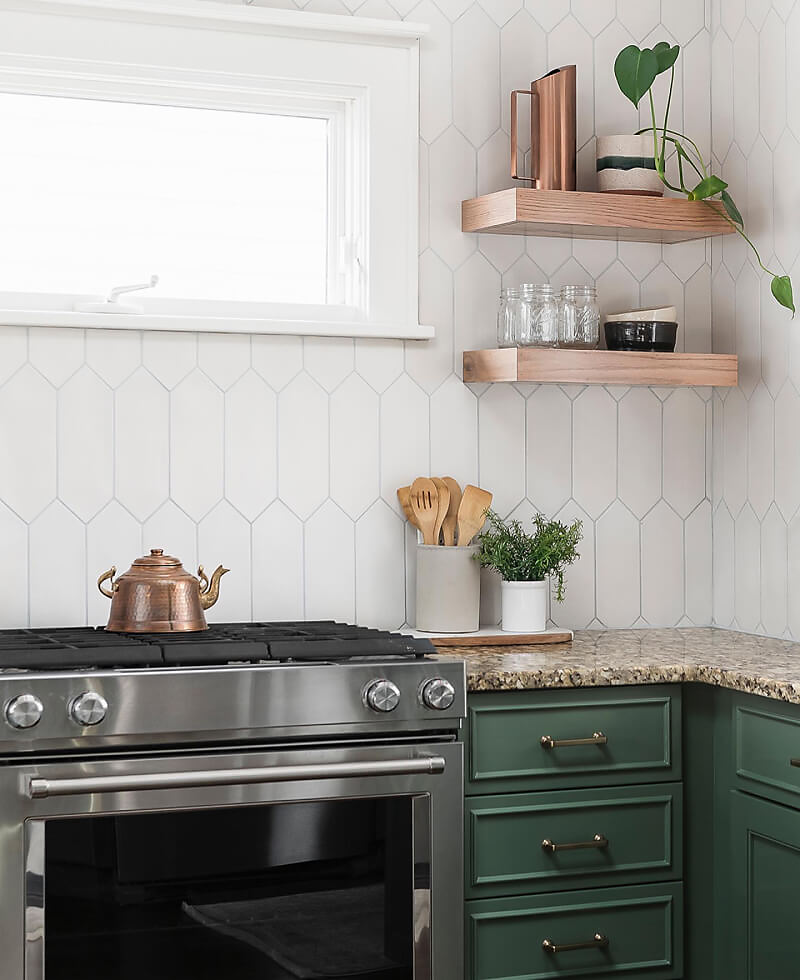 A kitchen with dark green cabinets and a white backsplash, featuring a KitchenAid® slide-in range.