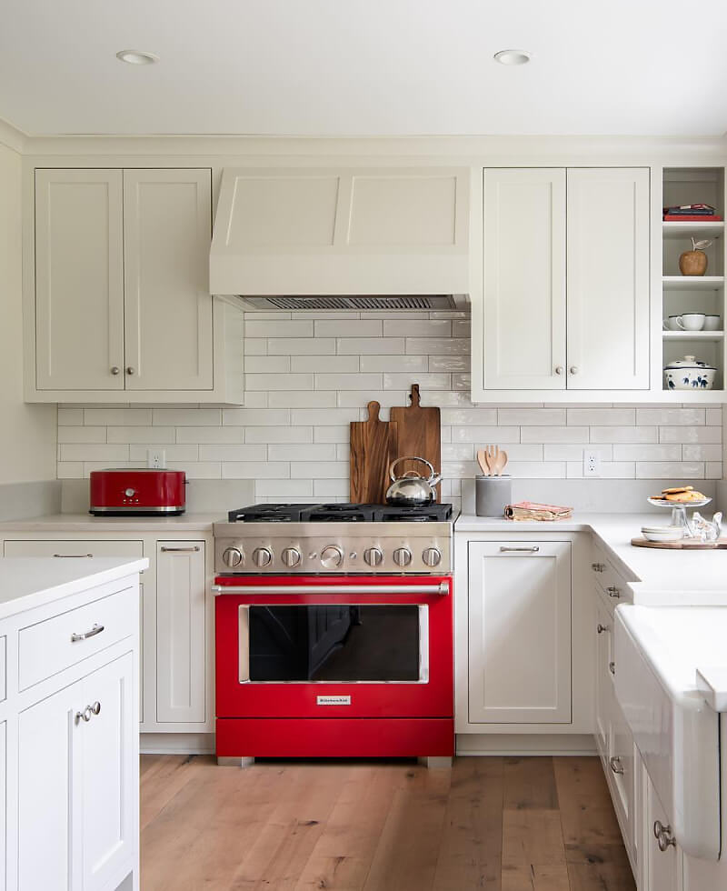 A white kitchen with subway tile featuring a red KitchenAid® commercial-style range.