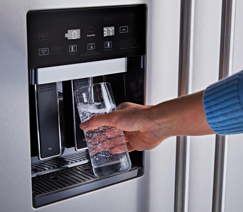 A person filling a glass of water with the External Water Dispenser on the KitchenAid® Built-In Side-by-Side Refrigerator