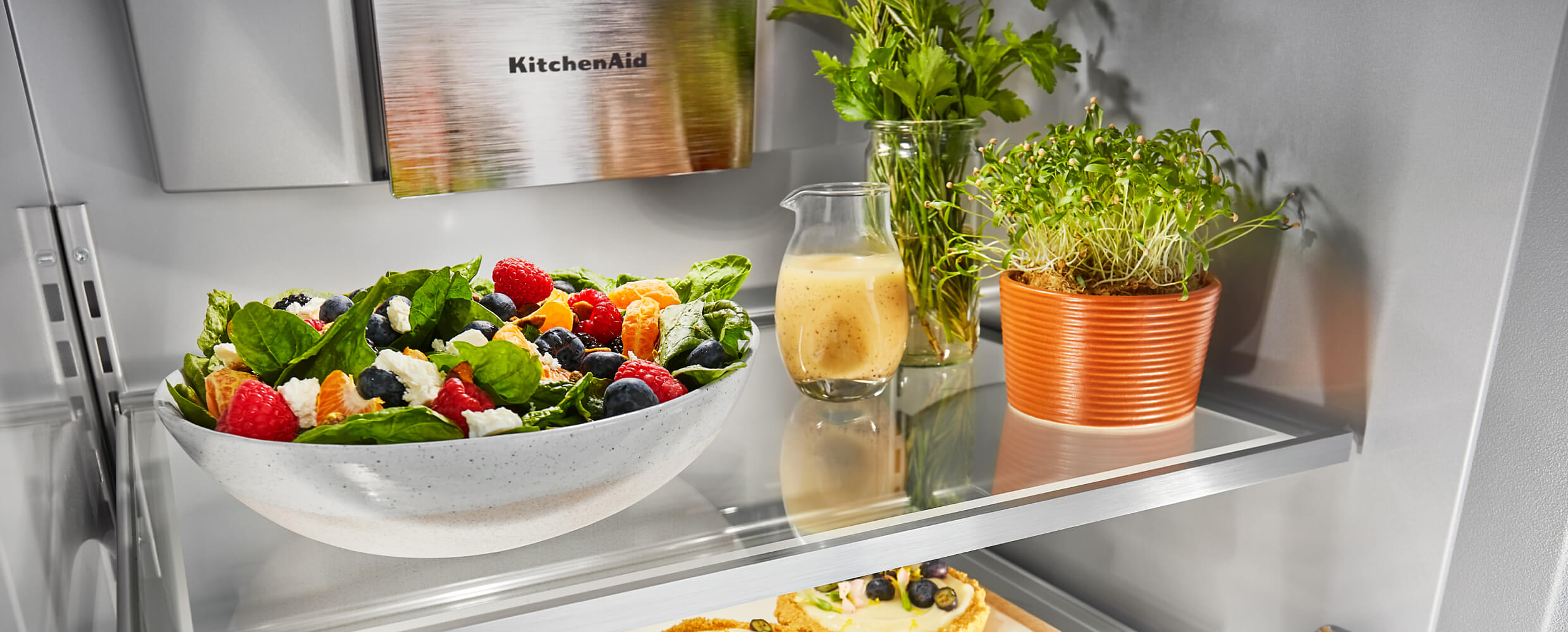 Interior of a 48" KitchenAid® Built-In Side-by-Side Refrigerator filled with a large fresh salad, beverages and herbs