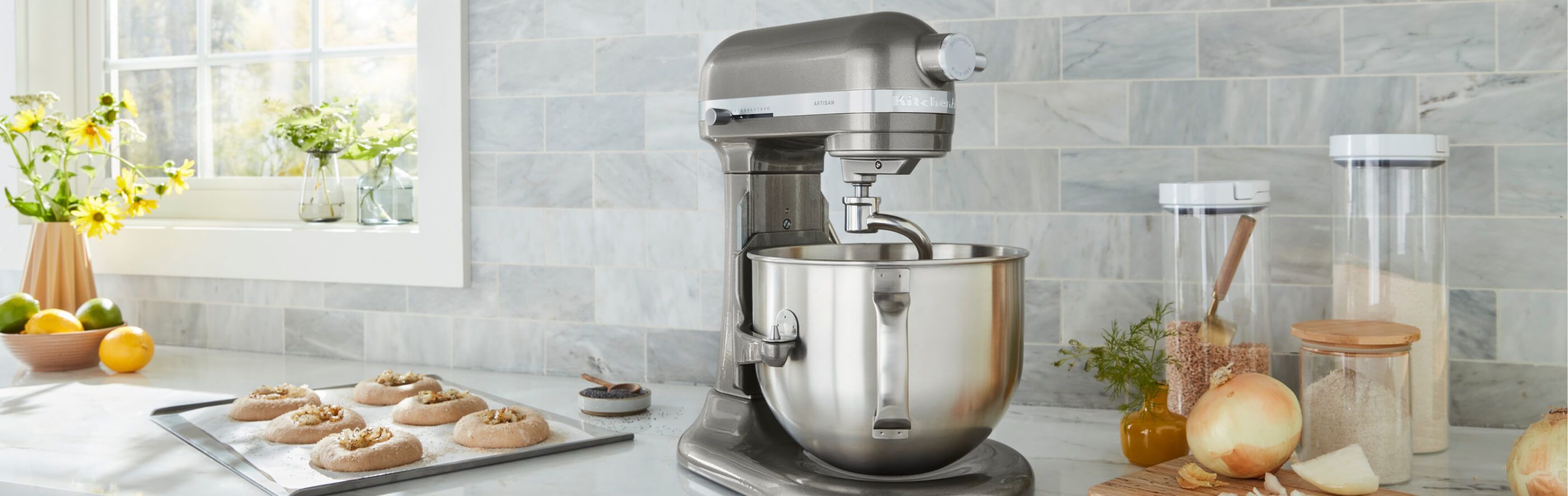 A KitchenAid® Bowl-Lift Stand Mixer on a countertop, with prepared pastries and different ingredients in glass canisters. 