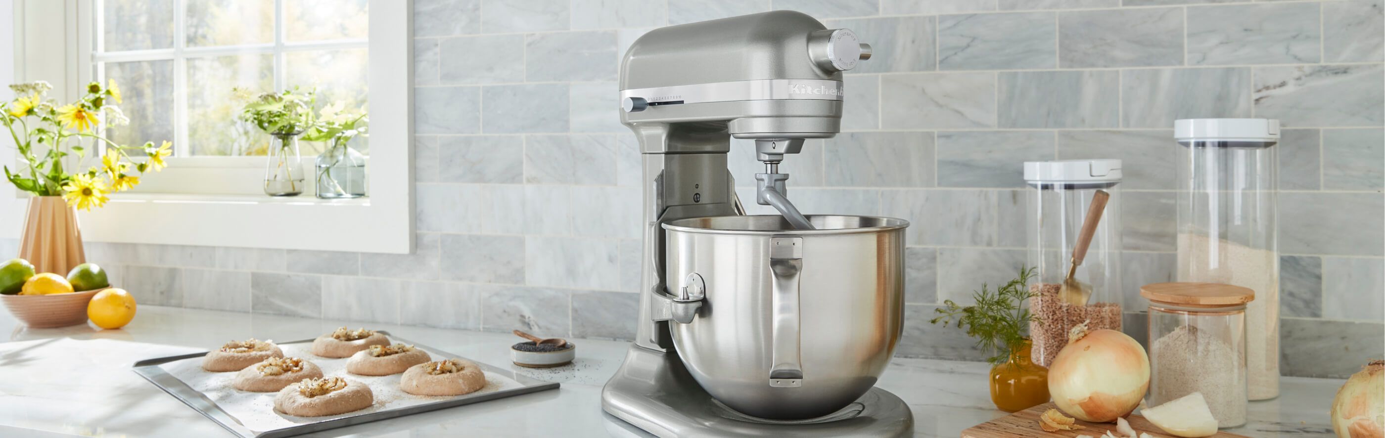 A KitchenAid® Bowl-Lift Stand Mixer on a countertop, with prepared pastries and different ingredients in glass canisters.