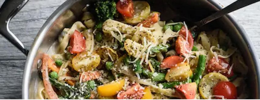 Pasta primavera in a bowl garnished with basil and parmesan cheese.