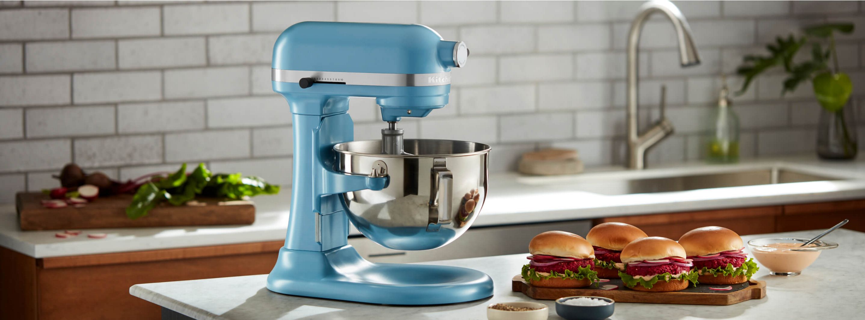 A KitchenAid® Bowl-Lift Stand Mixer on a countertop with prepared beetroot burgers on a countertop next to the mixer. 