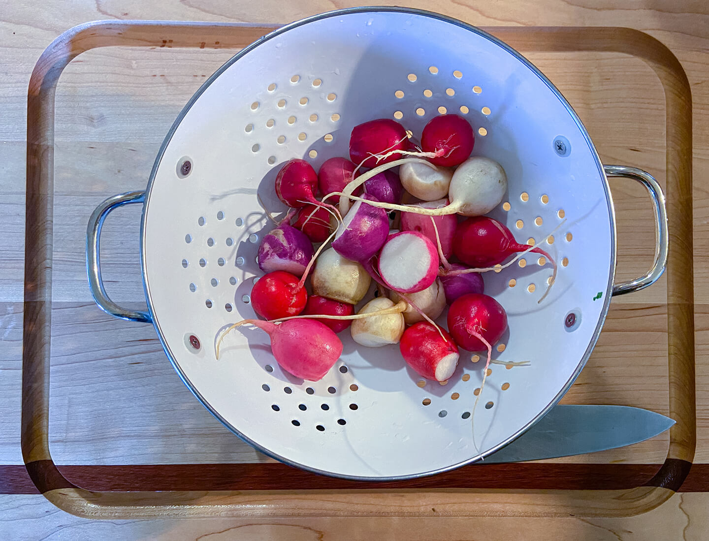 A metal strainer filled with freshly cleaned, whole radishes.