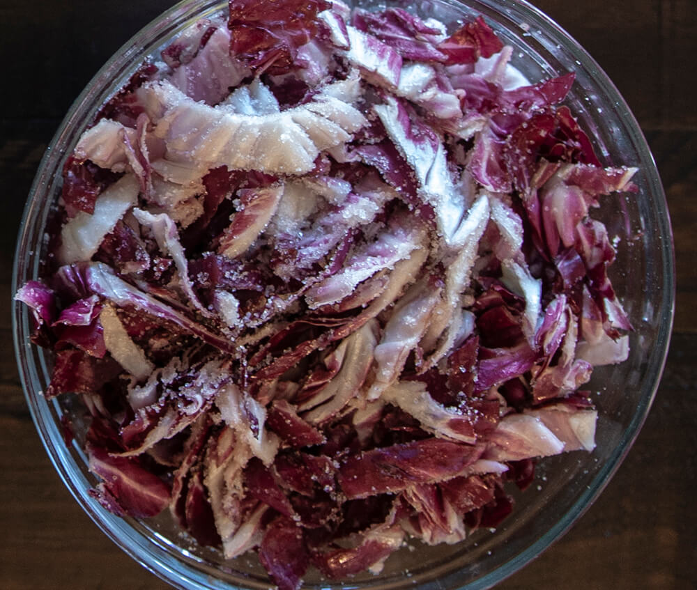 A glass bowl filled with sliced, salted red cabbage.