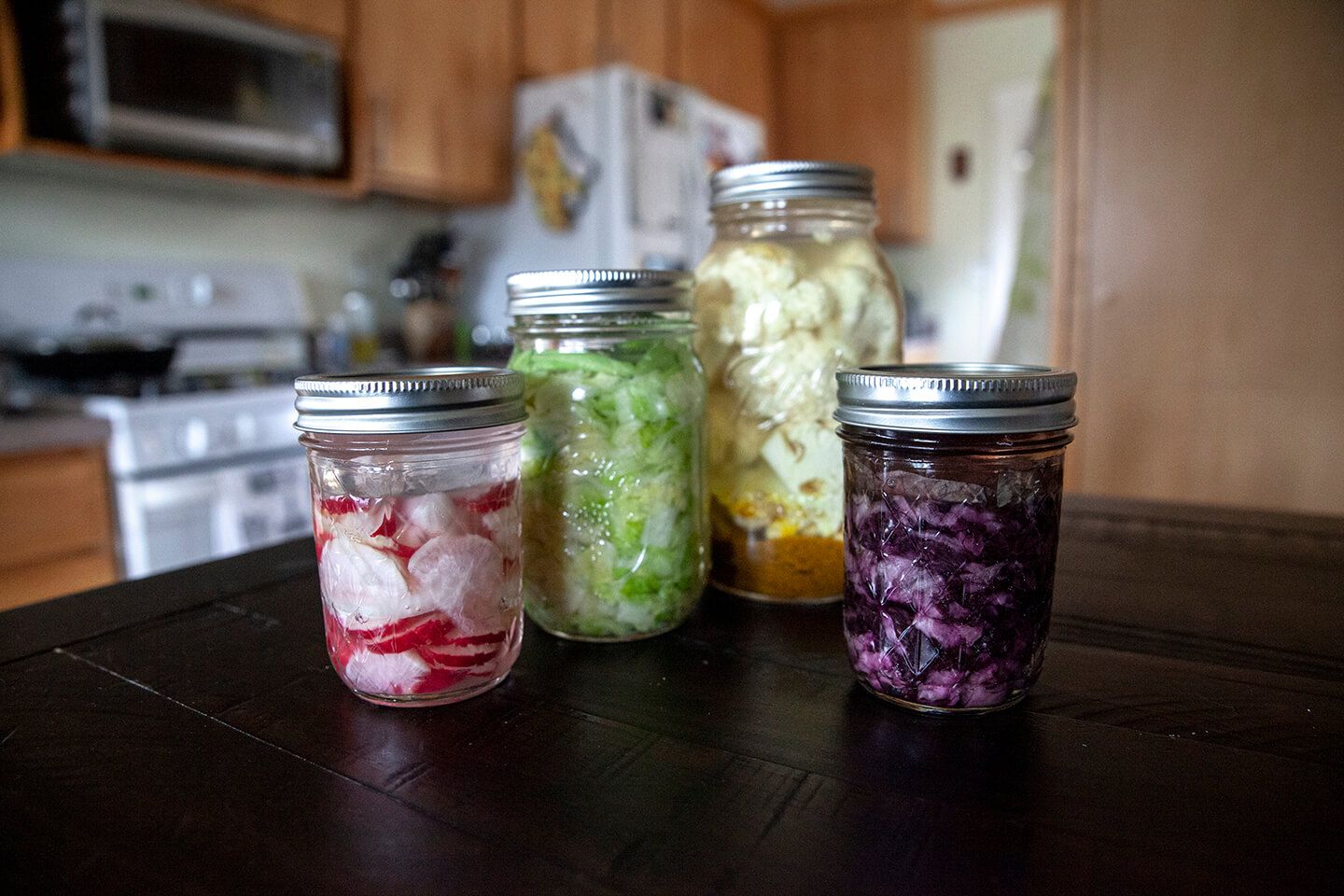 Four sealed, glass jars holding a variety of fermented vegetables.