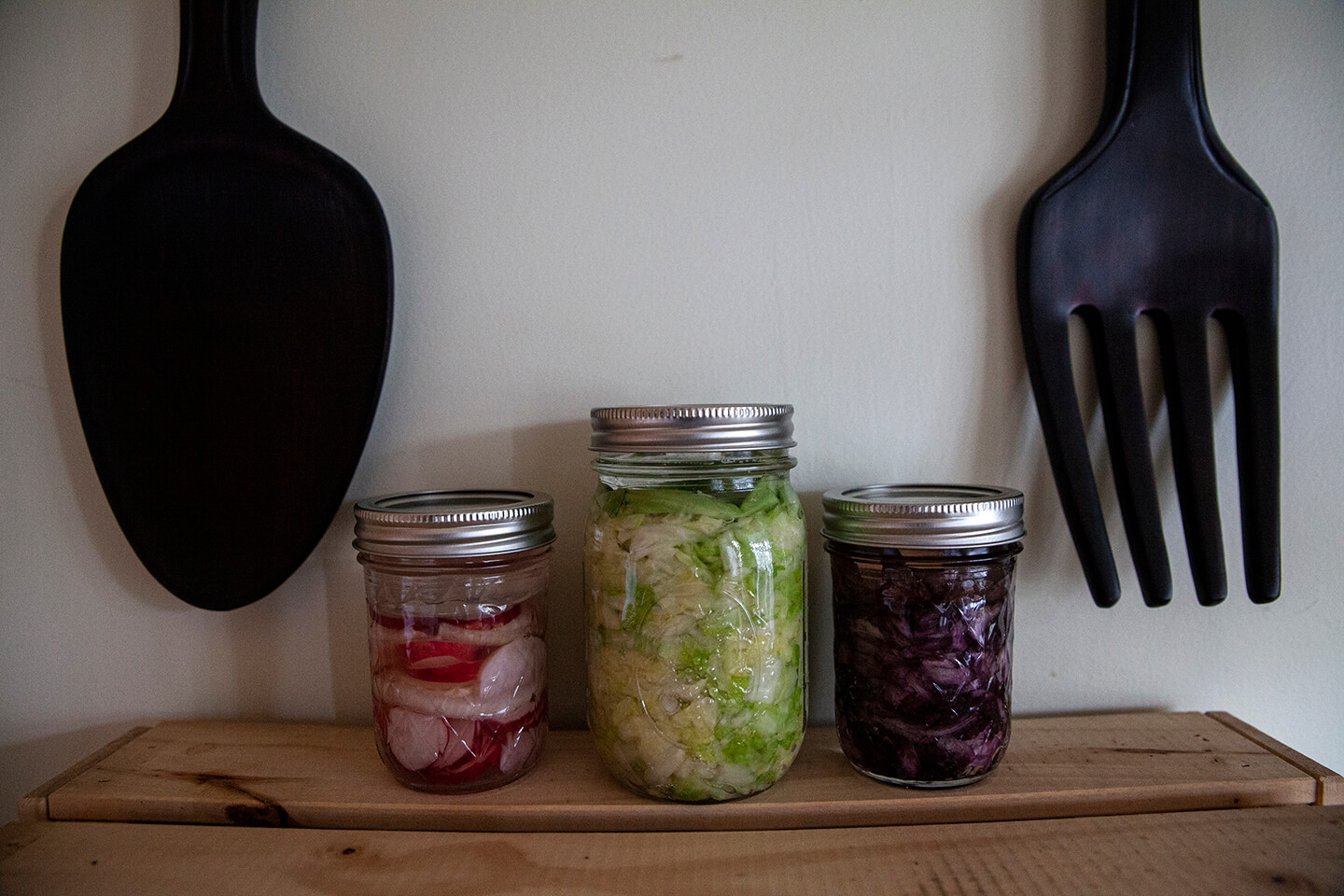 Three glass jars holding fermented radishes, red cabbage and green cabbage.