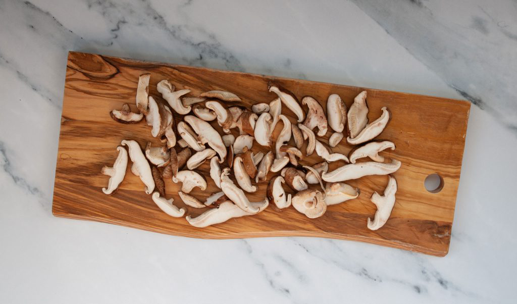Sliced mushrooms resting on a wooden cutting board.