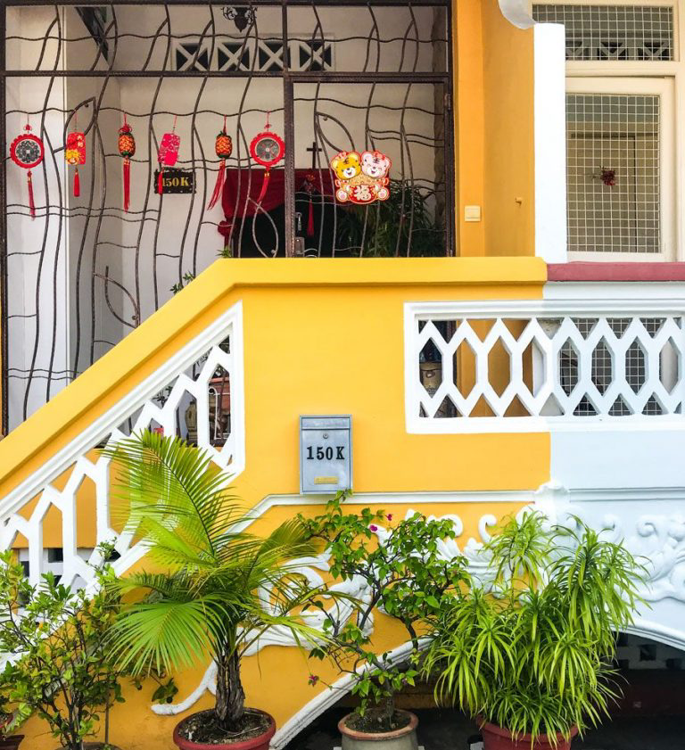 The bright yellow exterior of a home with various plants and Lunar New Year decorations hanging.