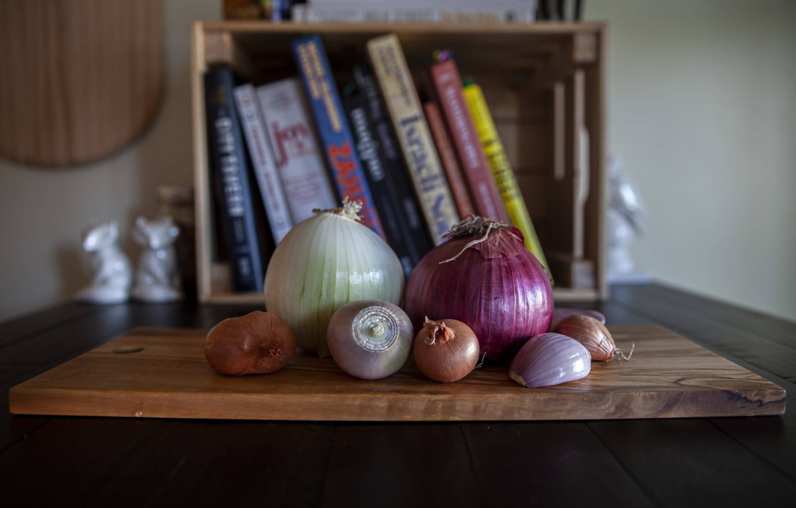 Assorted onions of all shapes and sizes resting on a wooden cutting board.