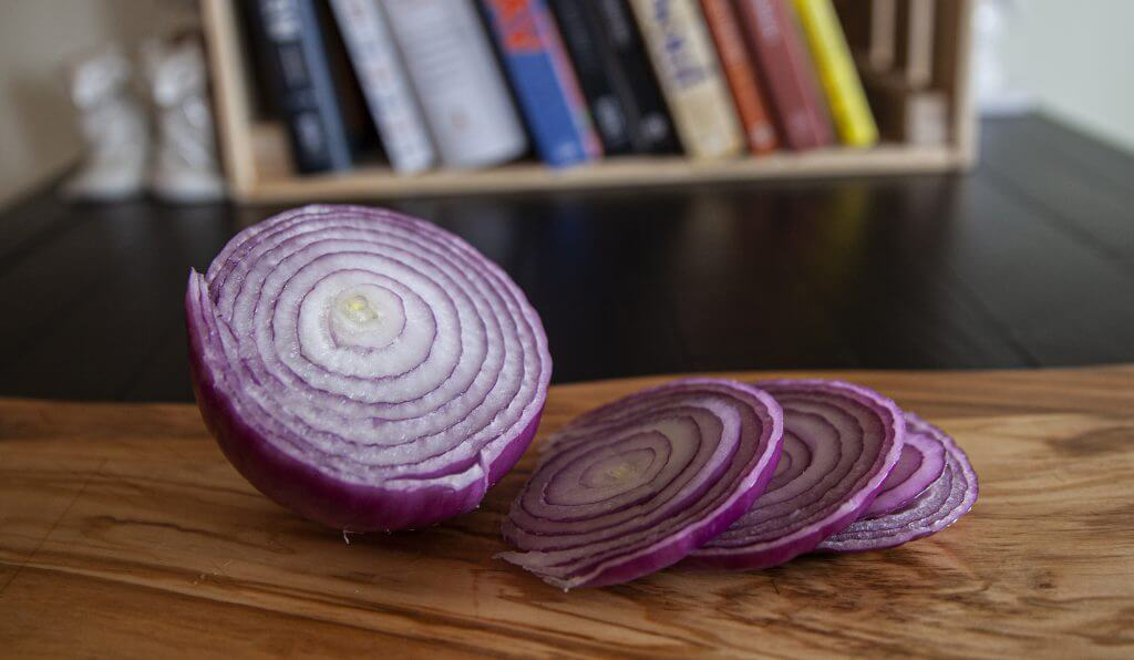 A sliced red onion resting on a wooden cutting board.