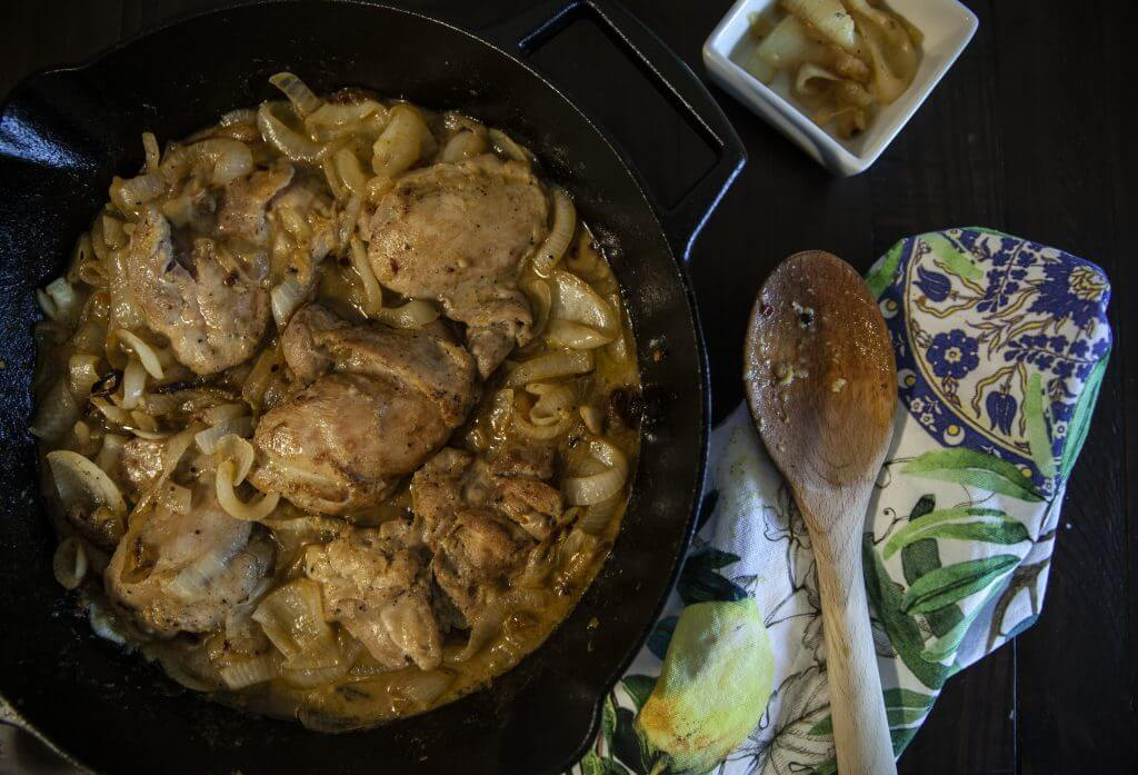 Chicken thighs cooking in a cast iron skillet with caramelized onions.