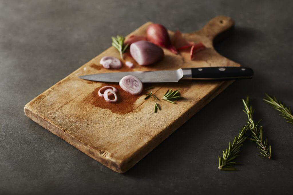 Sliced onions and thyme resting on a wooden cutting board.