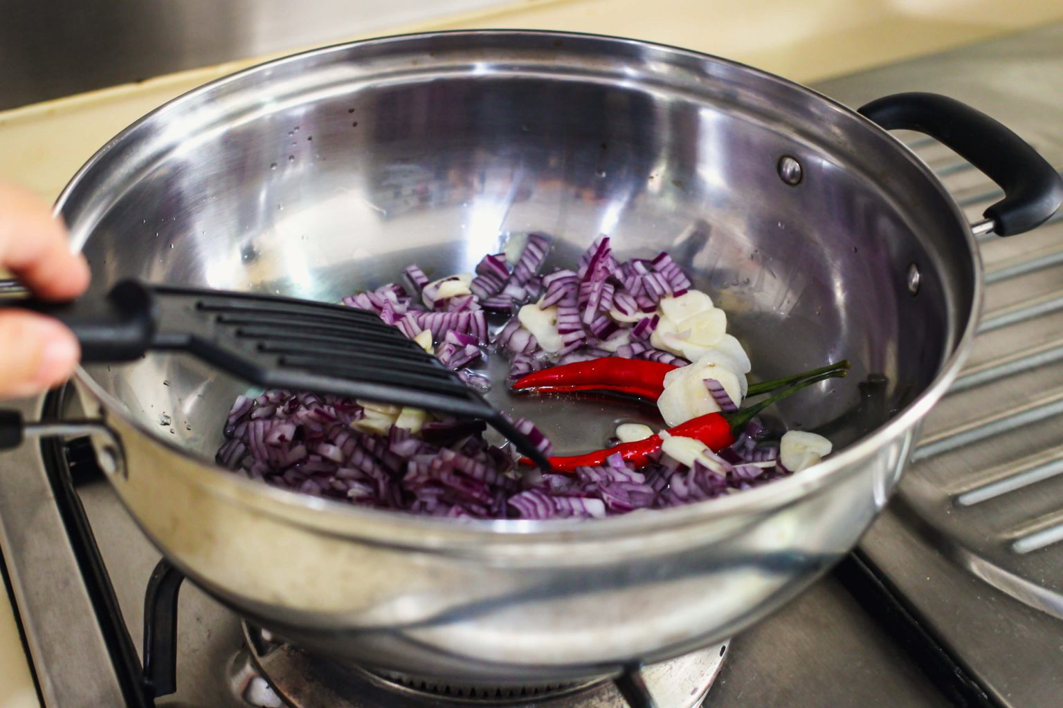 A pan sautéing diced red onion, garlic and peppers.
