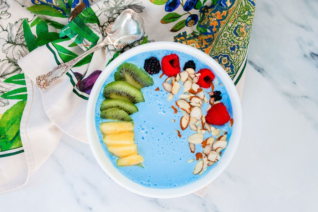 A blue smoothie bowl filled with sliced fruits and chopped nuts.