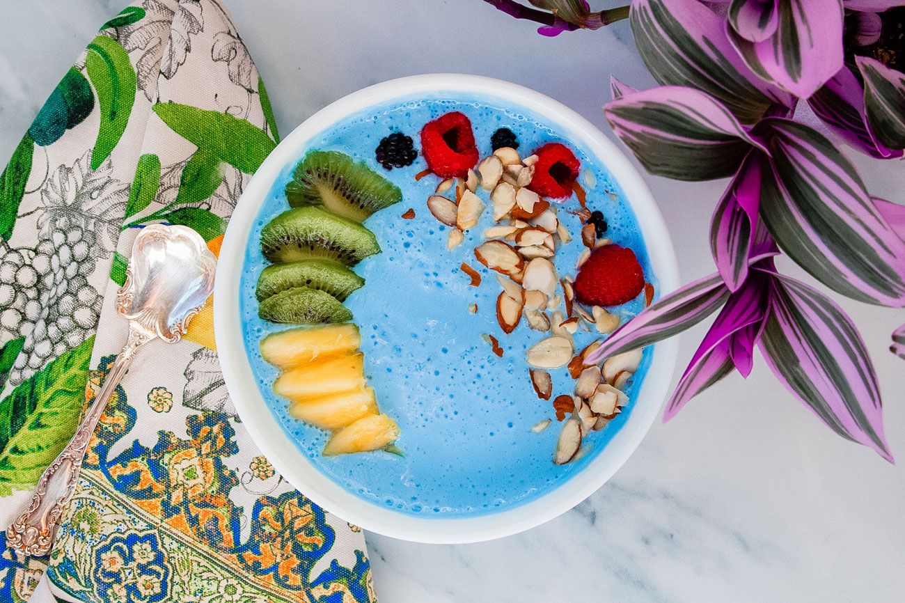 A blue smoothie bowl filled with sliced fruits and chopped nuts.