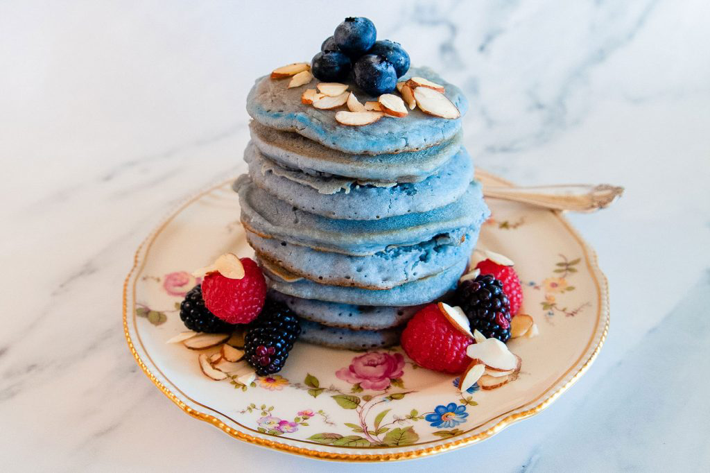 A small delicate plate towering with blue pancakes.