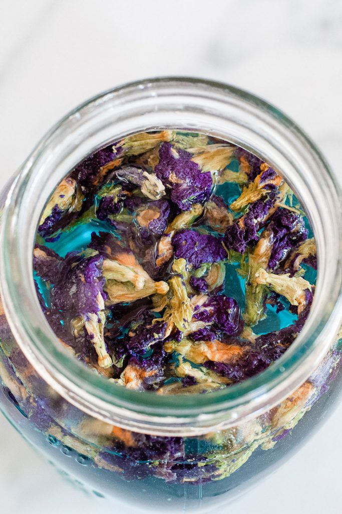 A glass jar filled with soaking butterfly pea flower petals.