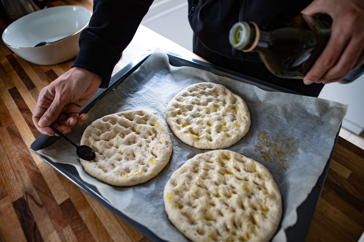 A person dressing focaccia bread with olive oil.