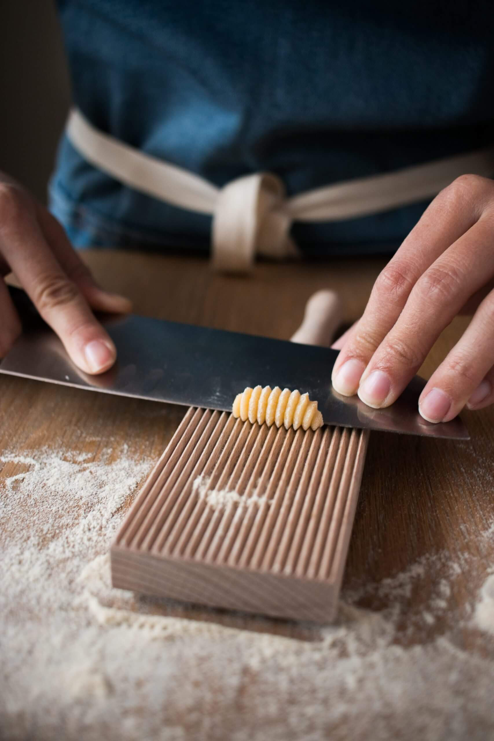 Experienced hands rolling out homemade gnocchi on a gnocchi roller board with a chef's knife.