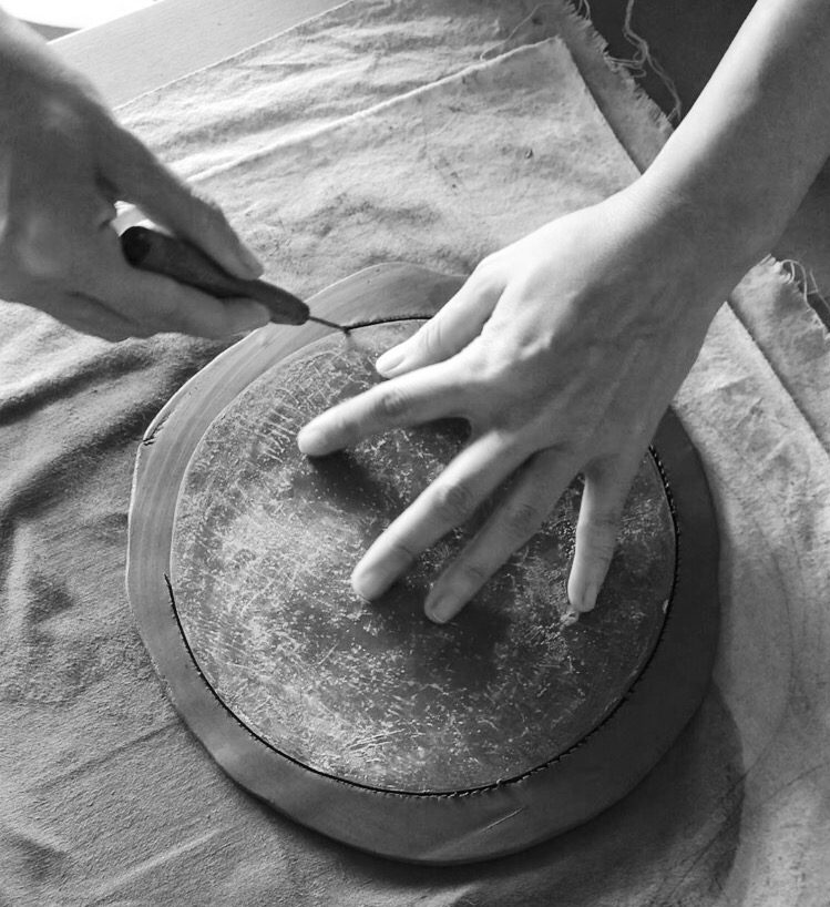 A hand gently trimming clay around a flat disc.