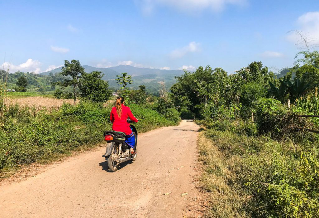 A woman riding a motorized scooter through rural Myanmar.