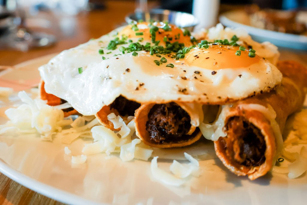 A plate of taquitos topped with a fried egg.