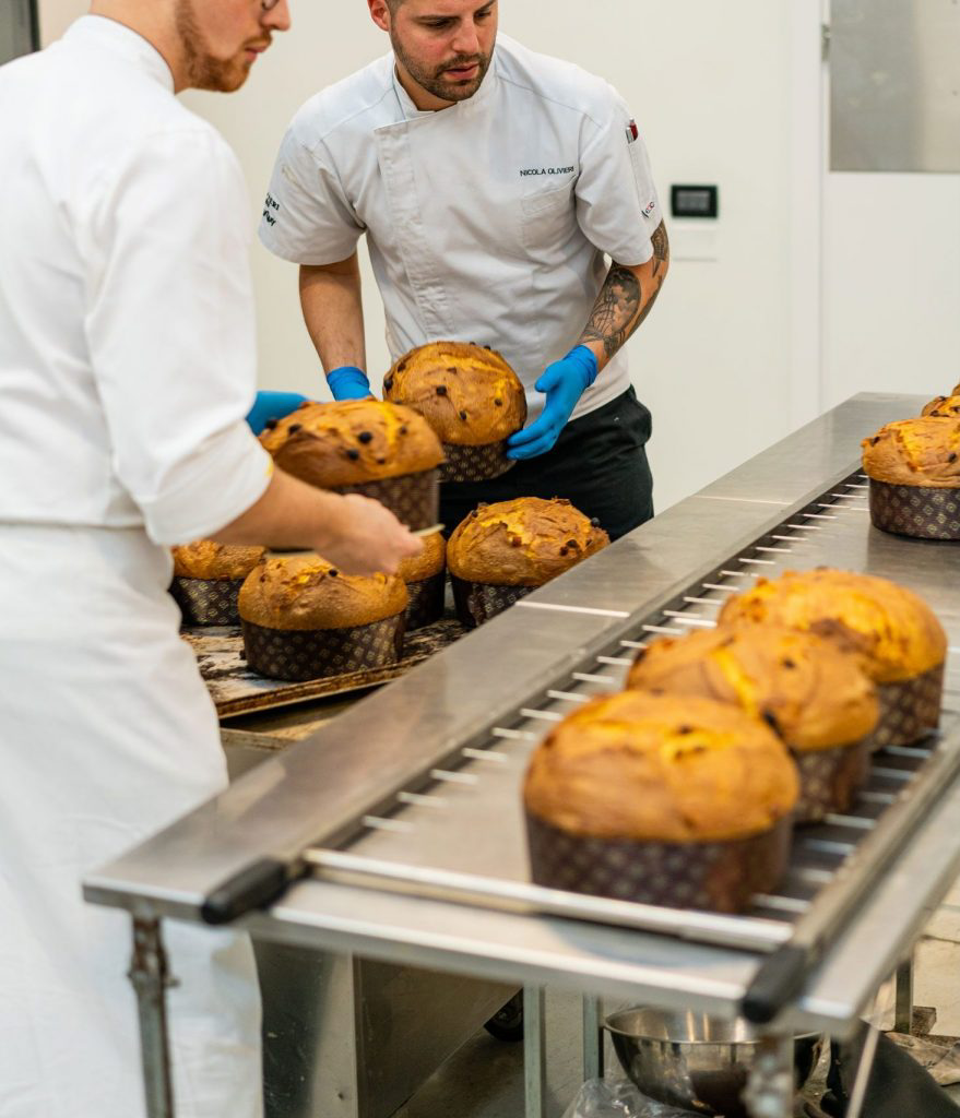 Bakers delicately handling baked panettones on an assembly line.