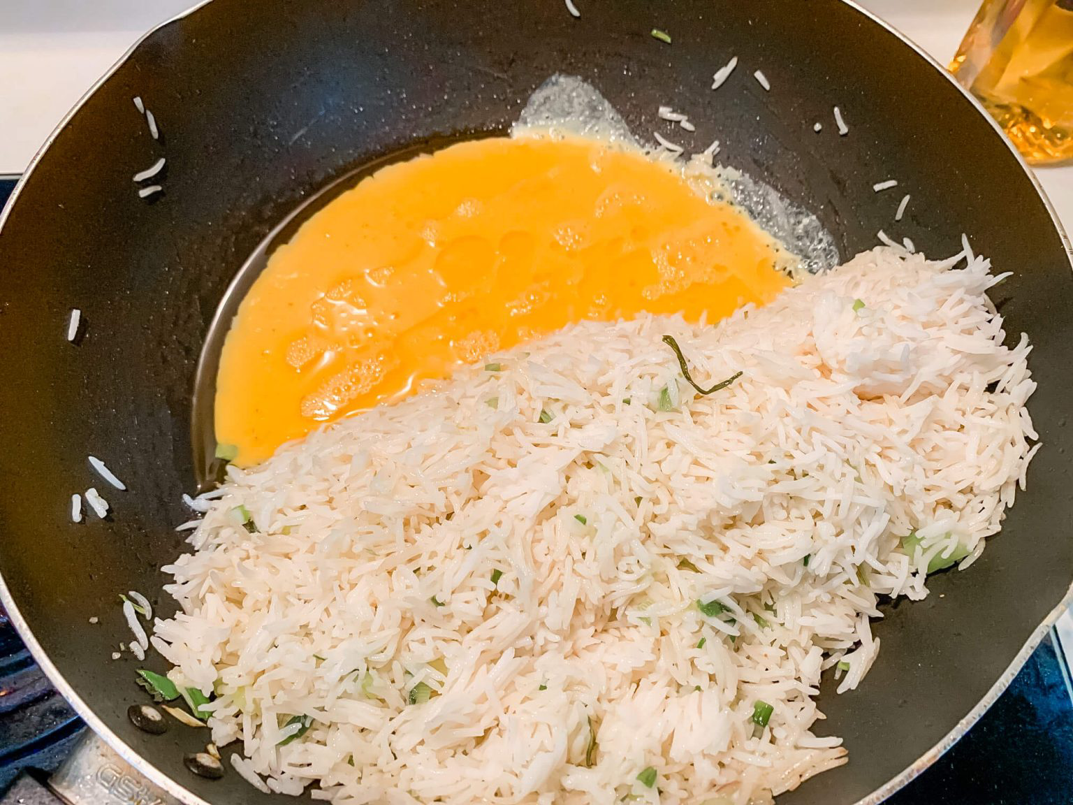 Egg, white rice and green onions frying in a wok.