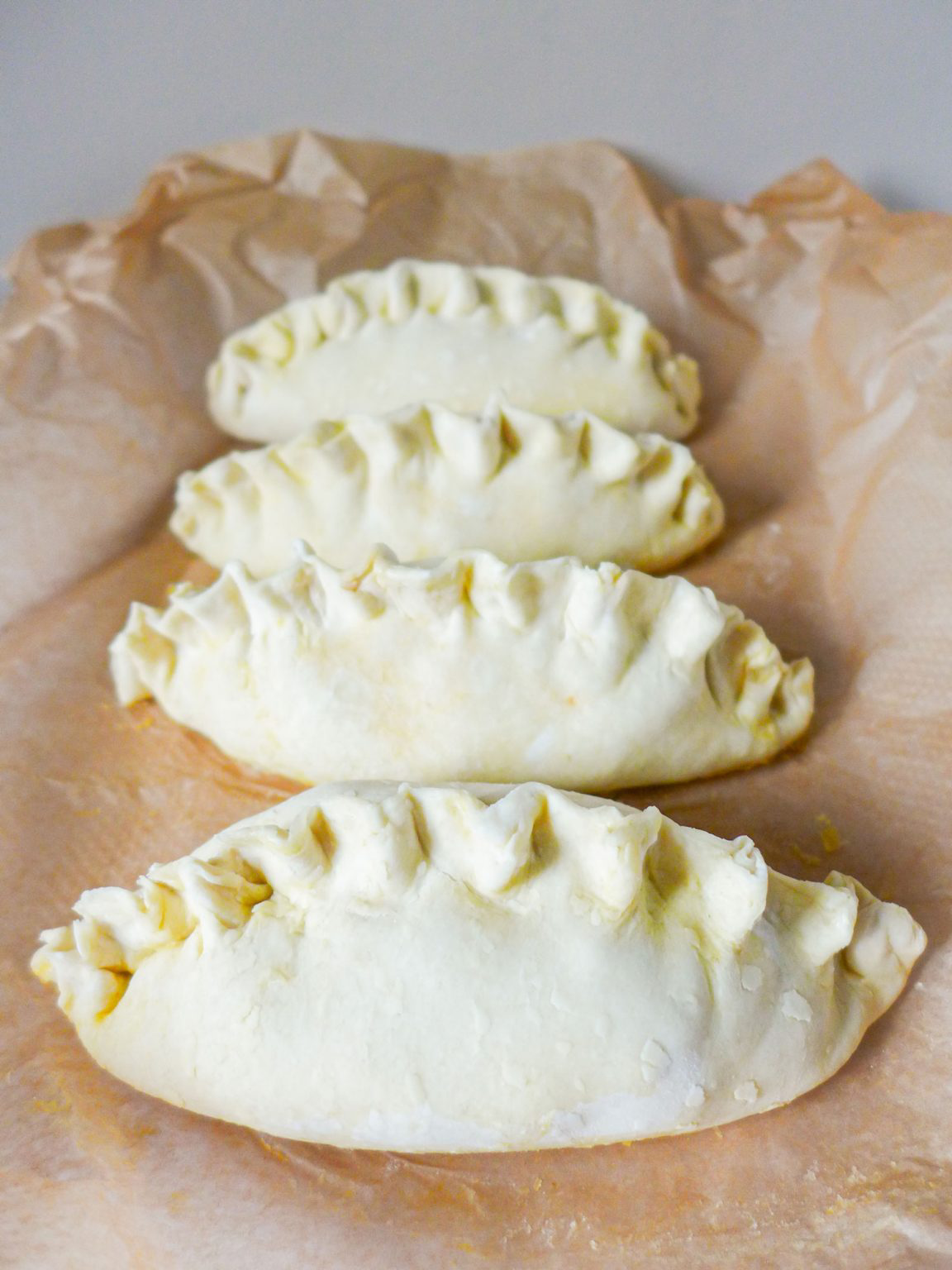Four uncooked crab pasties resting on parchment paper.