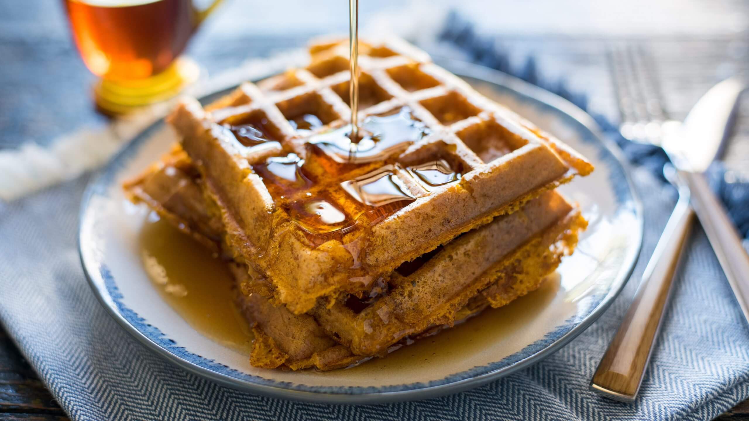 A close-up of freshly made, crispy waffles being doused in in silky syrup.