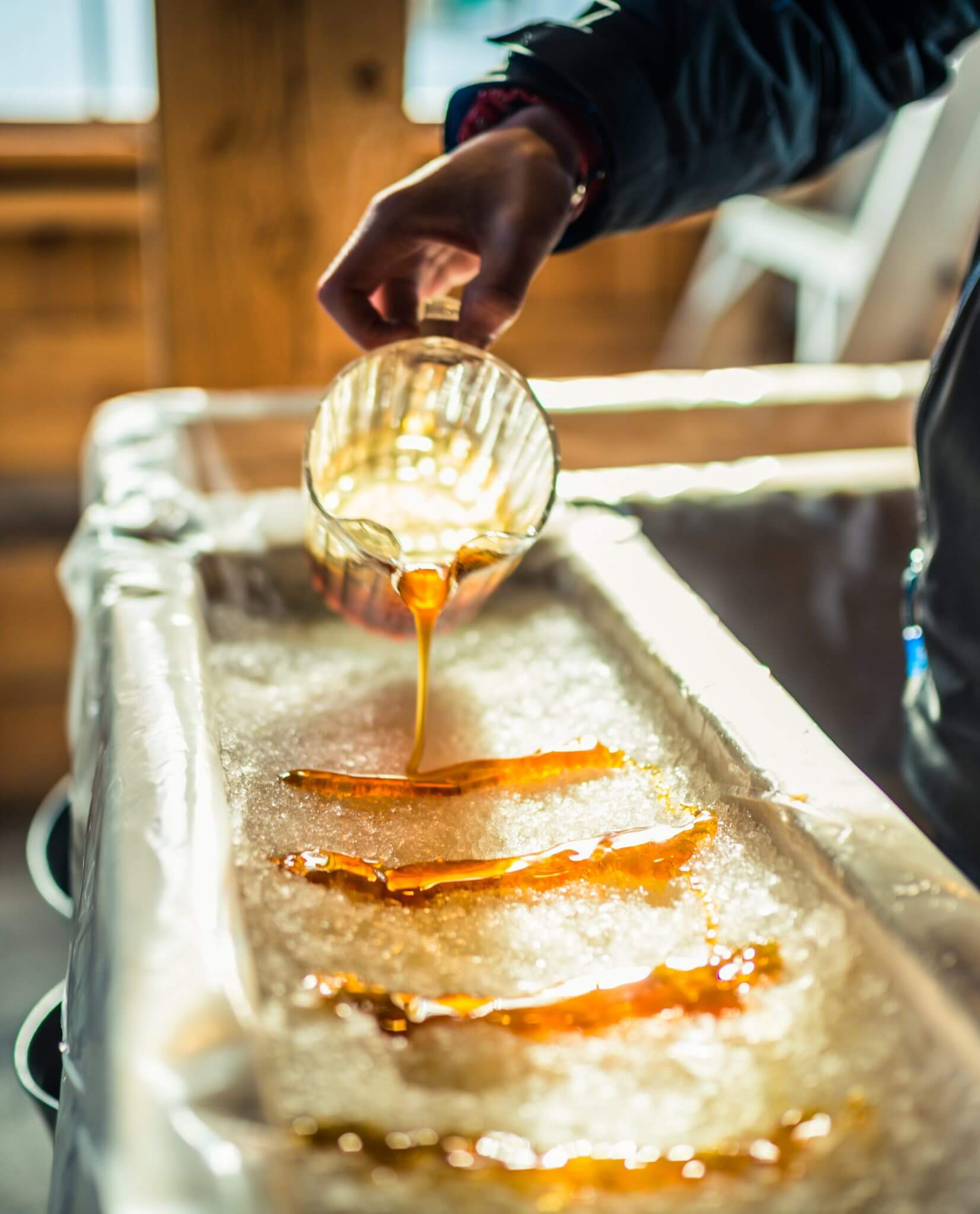 A close-up of a person gently pouring rows of syrup into packed snow for a sweet treat.