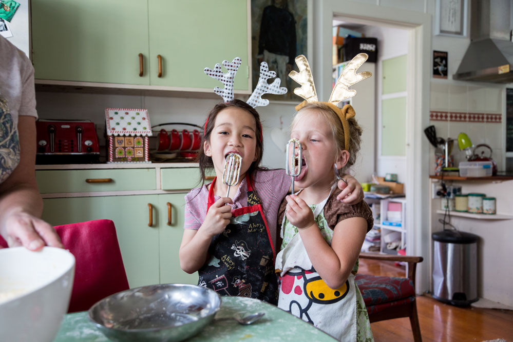Two young children licking batter off of mixing beaters.