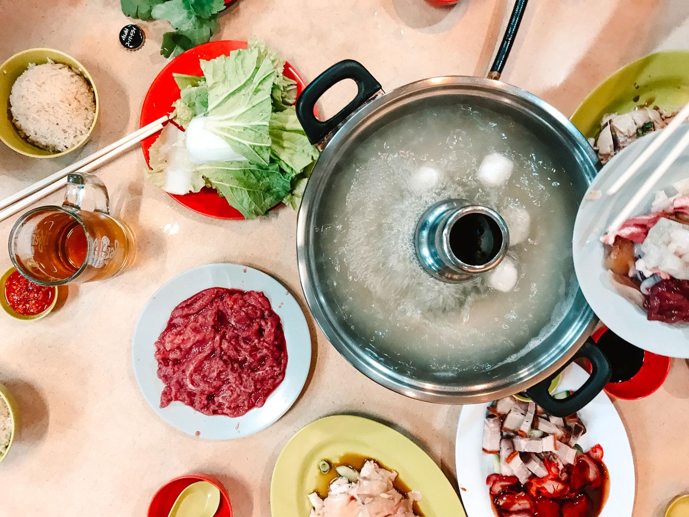 A boiling steamboat surrounded by raw vegetables and meats.