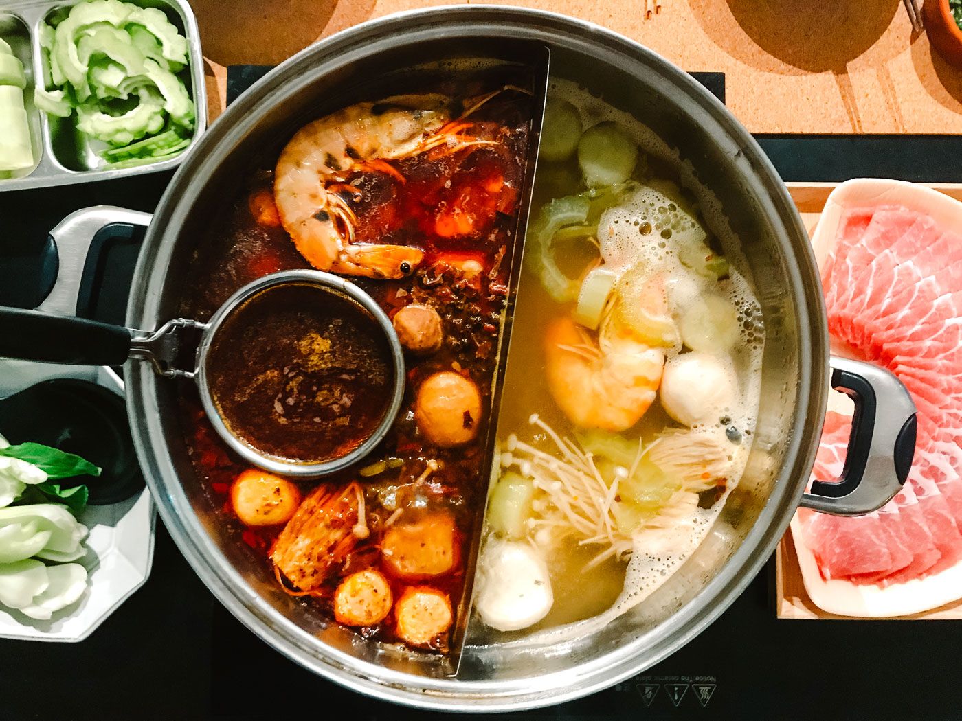 A steamboat, or hotpot, resting on a table with various raw ingredients.