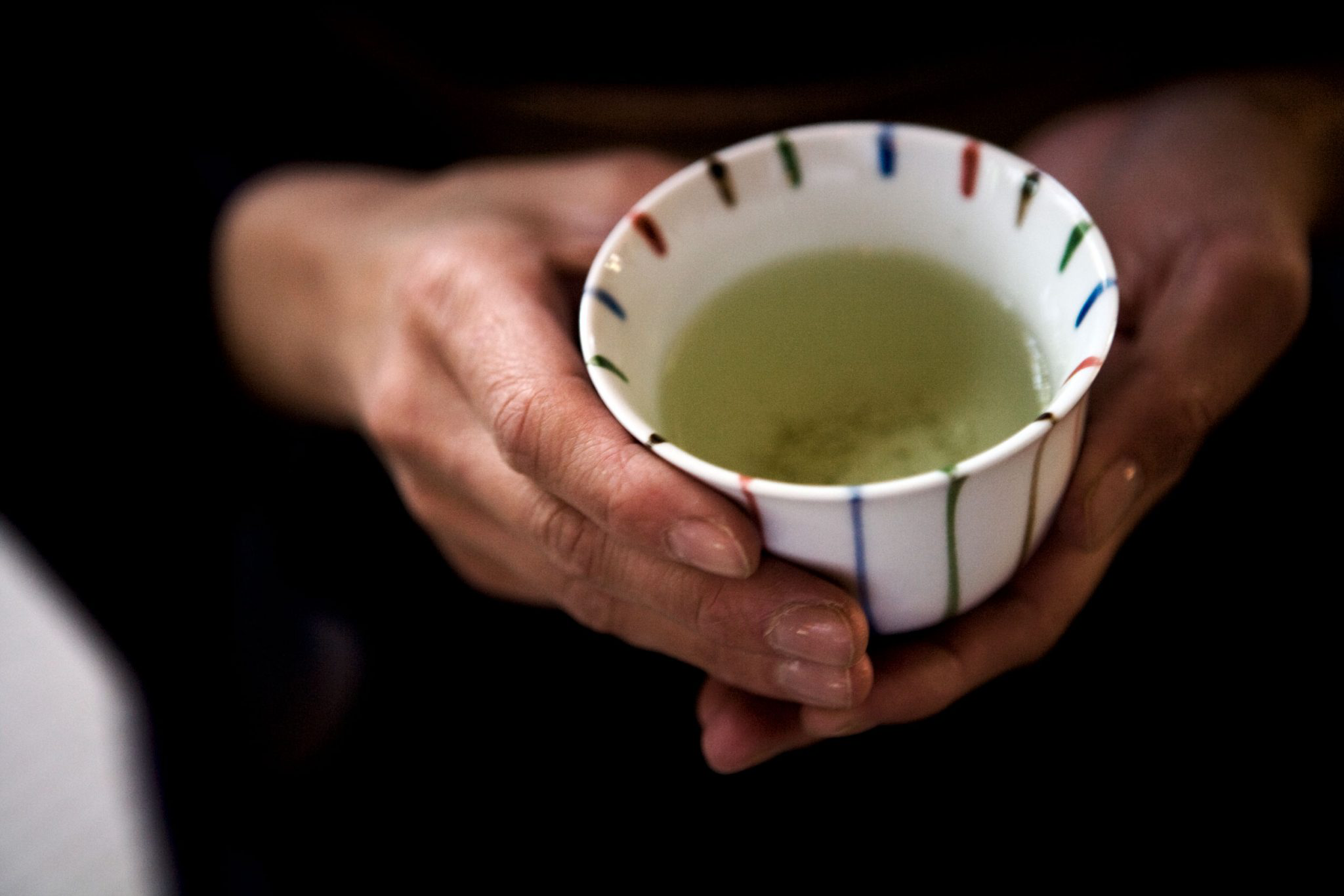 Calm hands holding a small ceramic cup filled with green tea.