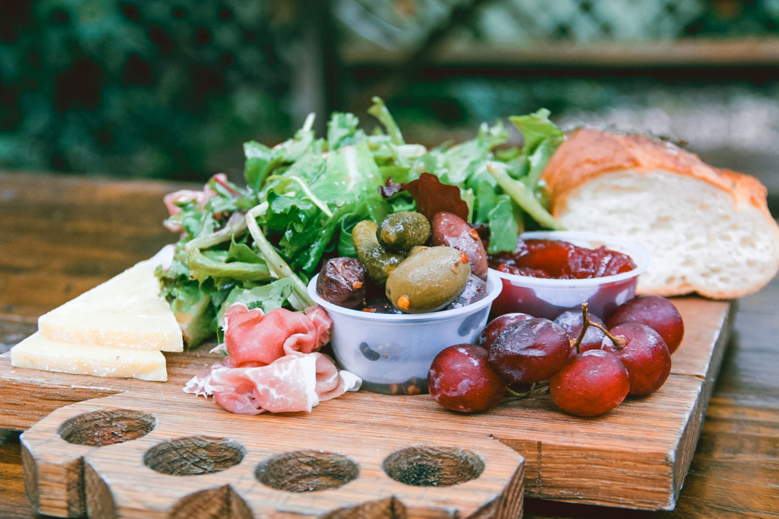 Meat and cheese board with bread, lettuce and grapes.