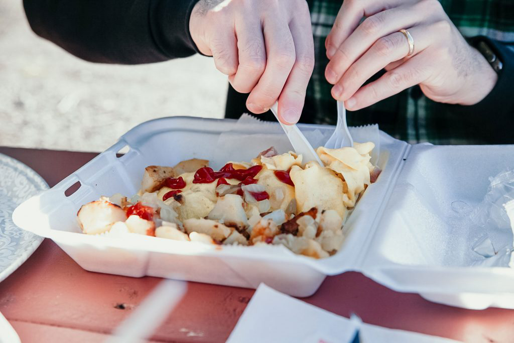 A person digging into their takeaway container of food with a knife and fork.