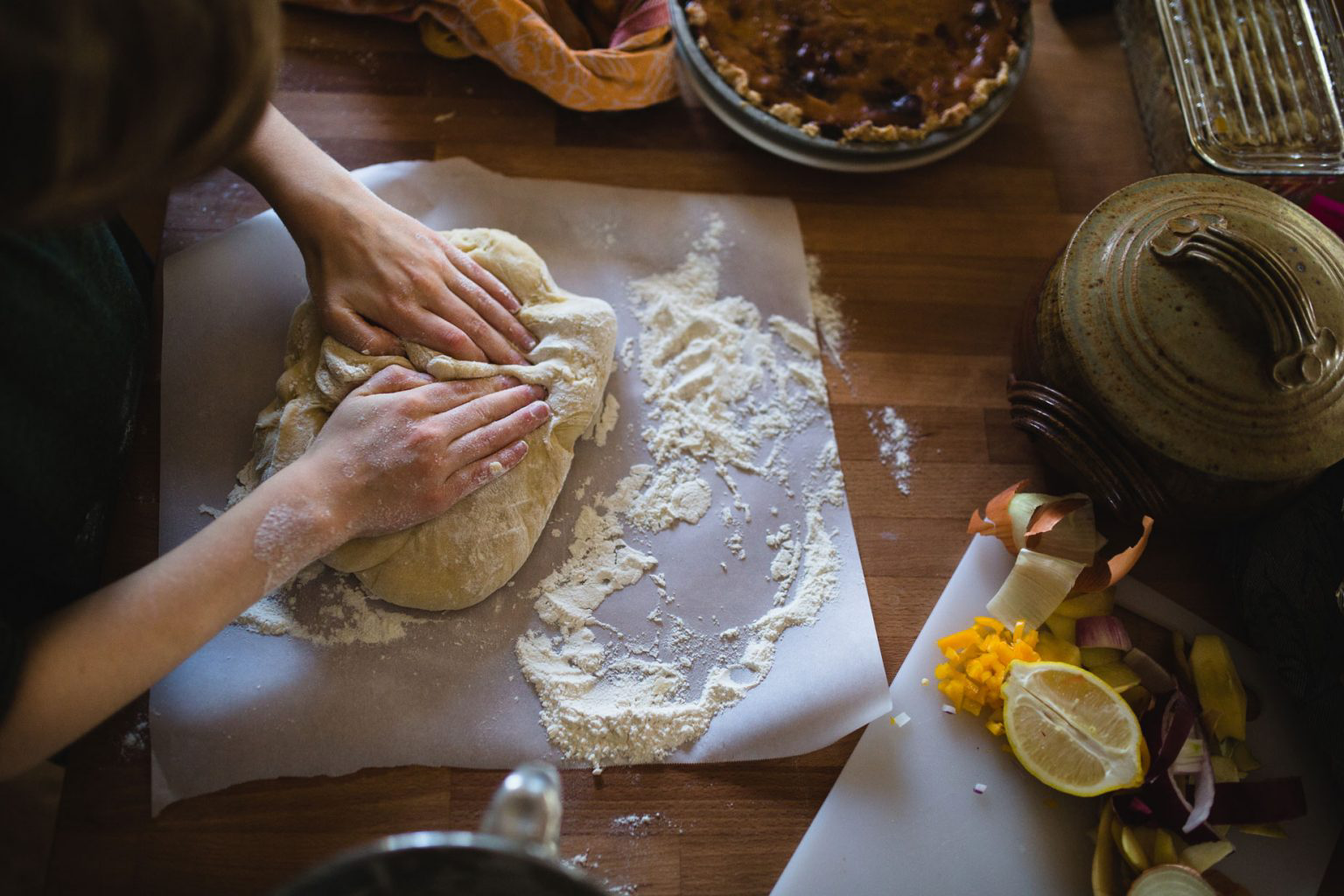 A person kneading dough with flour on a sheet of parchment paper.