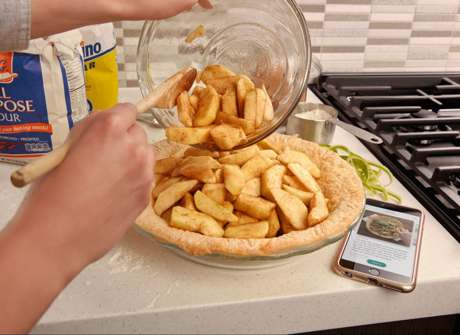 A person pouring apple slices into a pie crust in a glass dish.